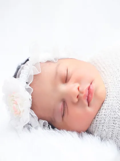 The face of an angel. This close-up in a white floral headband shows the perfect, peaceful expression of a sleeping newborn.