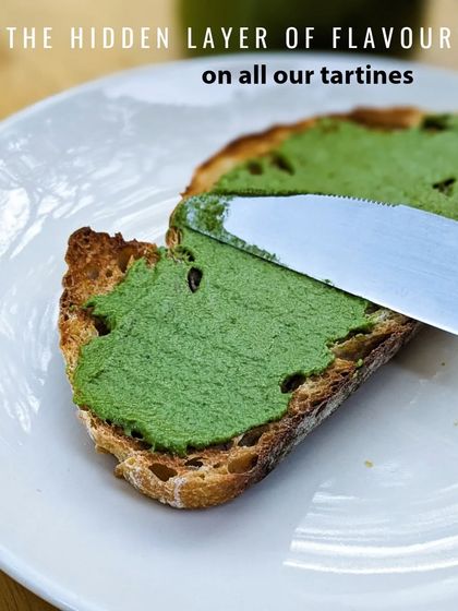 Revealing the secret to our tartines: a hidden layer of our house-made coriander pesto. It adds a fresh, herby kick to every bite.
