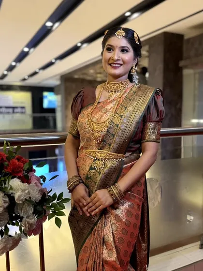 A full-length shot of a South Indian bride in a beautiful Kanjeevaram saree with puffed sleeves. Her makeup is classic and regal.