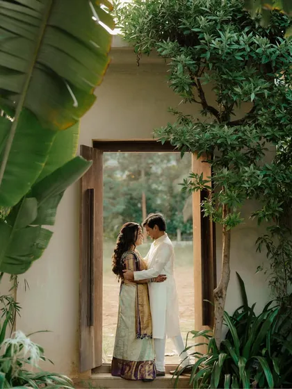 A couple shares an embrace in a doorway, framed by lush green trees. This romantic portrait uses natural elements to create a beautiful and intimate composition.