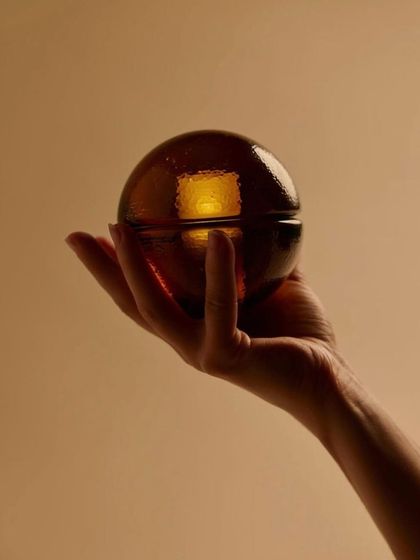 A hand holds the sepia-colored Bocci 14p, giving a sense of its satisfying, palm-sized form and portability.