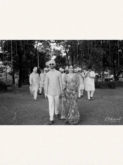 A black and white photograph of the bride and groom walking with their entourage, yet they are the clear focus. It captures the "marriage of equals" concept with a timeless, cinematic feel.