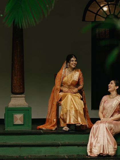 A bride and her bridesmaid share a happy, candid moment on the steps of a heritage building.