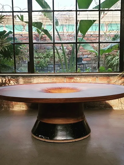This sculptural dining table features a solid wood top with a unique concave center, resting on a handcrafted ceramic and wood base. It is a perfect example of how we blend different materials to create a functional work of art.
