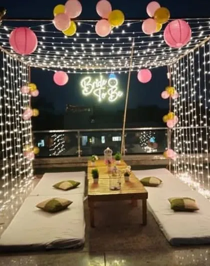 For a trendy and modern celebration, I can arrange a rooftop cabana like this one for a 'Bride to Be' party. The setup includes a canopy of fairy lights, comfortable low seating, a custom neon sign, and balloons to create a magical atmosphere.