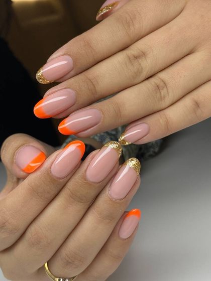 A fun and colorful French manicure. This design features a mix of bright orange and sparkling gold tips for a playful and festive look.