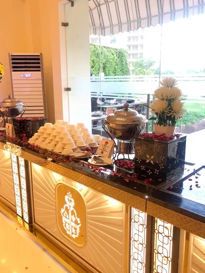 An elegant dessert and beverage counter from a recent event. The illuminated facade with a royal crest design, black marble top, and scattered rose petals creates a sophisticated and inviting display.