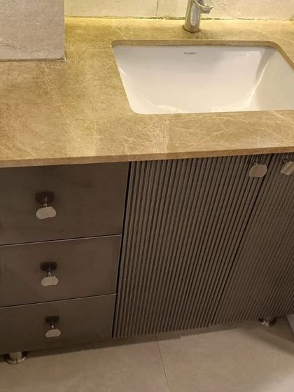 We designed this bathroom vanity to combine luxury and practicality. It features a marble countertop, sleek drawers, and a cabinet with a modern, fluted door, providing elegant storage for toiletries.