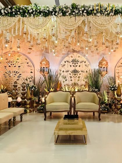 A full view of a magnificent stage, featuring a white carpeted aisle, elegant seating, and a backdrop of golden lotus motifs and hanging floral chandeliers.