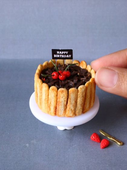A close-up of a miniature chocolate birthday cake, complete with tiny cherries.