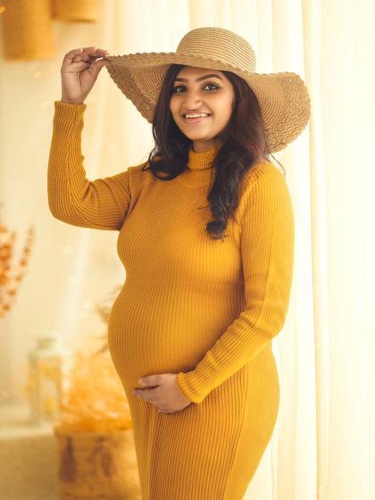 A chic and playful portrait of the mom-to-be in a stylish hat, her yellow dress glowing in the warm light.
