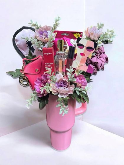 This unique gift arrangement for her features a large pink tumbler filled with beauty products like lip balm and perfume, a satin eye mask, and other fun accessories.