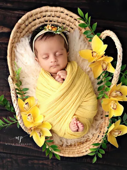 The definition of peaceful slumber. This newborn is swaddled snugly in a vibrant yellow wrap, nestled in a rustic basket and surrounded by beautiful matching flowers, showcasing our classic posed photography style.