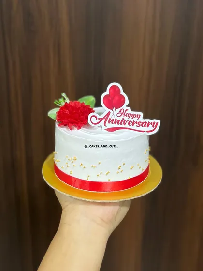 A sweet anniversary cake with a red ribbon and a festive topper.