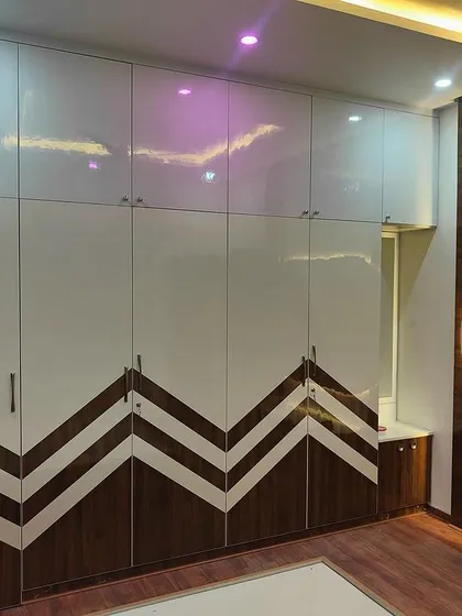 A full view of a master bedroom's storage solution, with a large wardrobe featuring a bold chevron wood inlay. This custom piece combines high-gloss white laminate with natural wood texture for a striking effect.