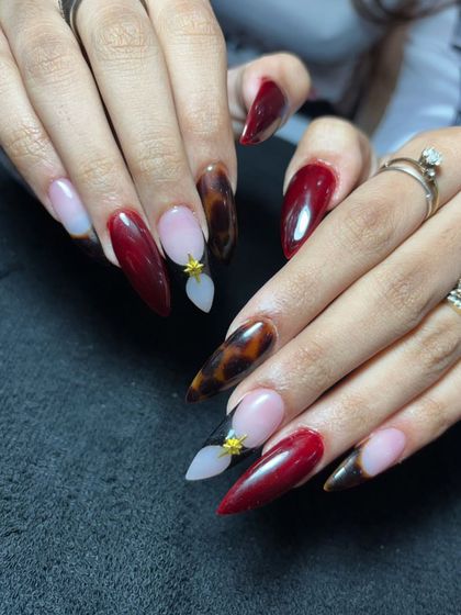 A dramatic stiletto set with a mix of deep red, tortoise shell, and nude nails with small 3D floral accents.