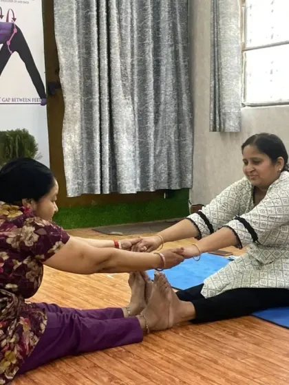 Partner work helps deepen stretches safely. Here, two students assist each other in a seated forward bend (Paschimottanasana), using gentle resistance to increase hamstring and back flexibility.