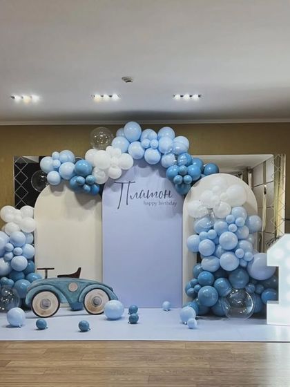 A stylish vintage car theme for a first birthday, featuring a blue and white balloon arrangement that looks like clouds and a large marquee number '1'.