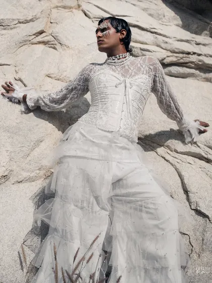 The all-white ensemble and makeup stand out beautifully against the textured rock face.