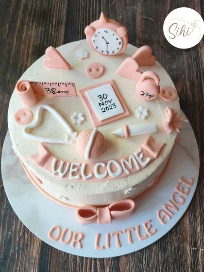 An adorable pastel baby-themed cake to welcome a precious little angel. It's covered in tiny, handcrafted fondant details like a clock, calendar, weight scale, and baby items.