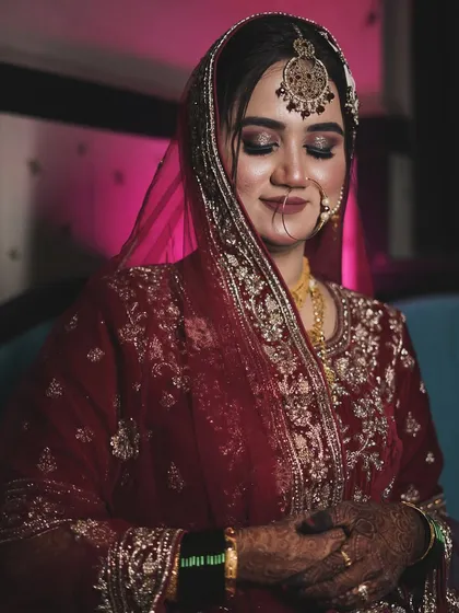 A moment of quiet reflection before the ceremony. The soft lighting highlights the glitter on her eyelids and the rich embroidery of her maroon dupatta.