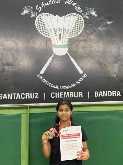 Shambhavi Kundgir with her runner-up medal from the team event at the MSSA Inter-School Badminton Championship, standing proudly in front of our academy banner.