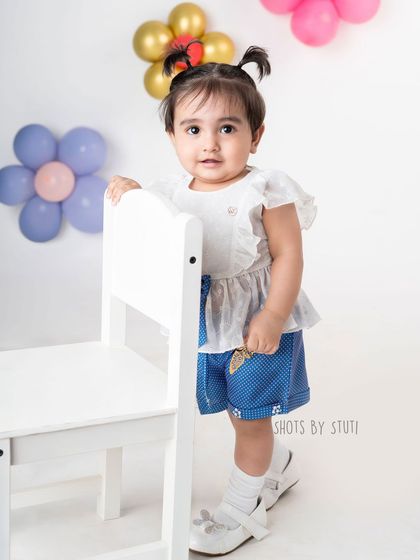 A playful and colorful outfit for a fun toddler portrait. The background with balloon flowers complements her look without overpowering her charming presence.