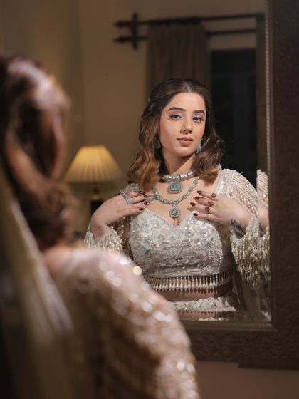 A moment of reflection. Our bride looks into the mirror, confident and beautiful in her engagement makeup and hair. The soft waves and glowing skin are perfect for the occasion.