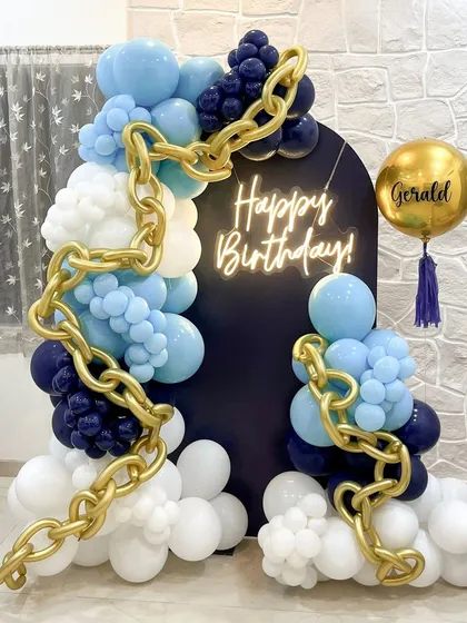 This setup shows a bolder, more masculine style for a birthday celebration. We used a palette of navy, light blue, and white balloons, weaving in a striking gold chain link sculpture that wraps around the custom 'Happy Birthday' neon sign.