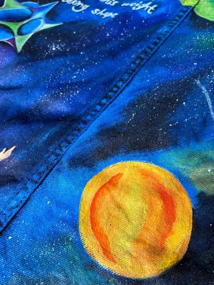 This shot highlights a painted planet and the star-dusted texture of the galaxy on the black denim. Each star is individually dotted to create a sense of depth and wonder.