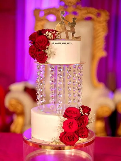 Our popular crystal chandelier wedding cake, beautifully lit against a vibrant pink background. The fresh red roses add a classic touch of romance.