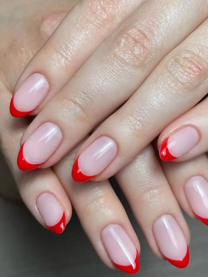 A classic French manicure with a twist, using a bright, glossy red for the tips on medium-length oval nails.