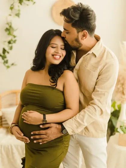 A classic and romantic maternity portrait of an expecting couple. The father-to-be gently kisses his partner's forehead, showcasing the love and anticipation in our signature boho style.