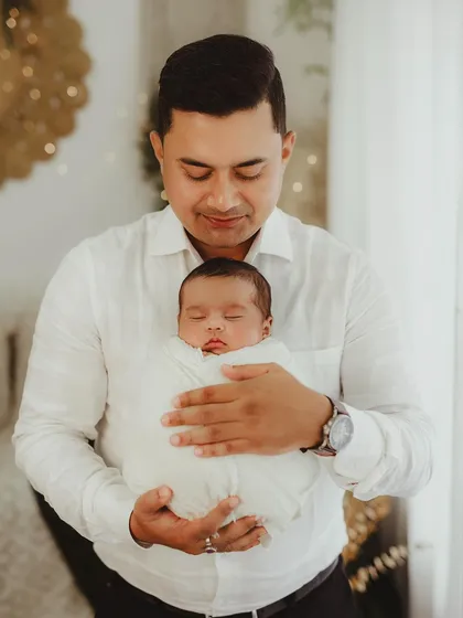 A father gently holds his swaddled newborn, a portrait of quiet strength and tenderness.