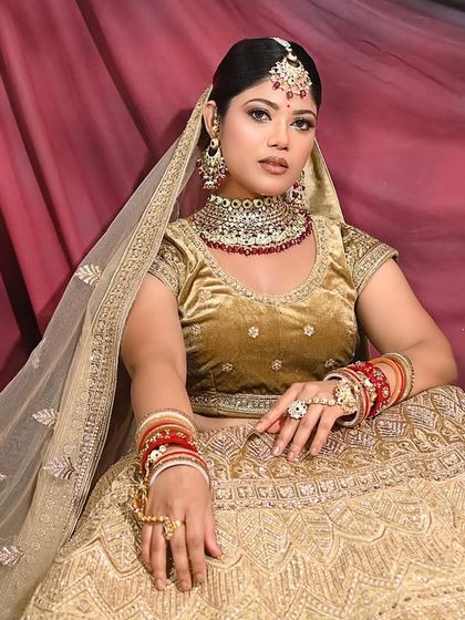 A full-length portrait showcasing the elegance of the golden lehenga against a dramatic red and black backdrop.