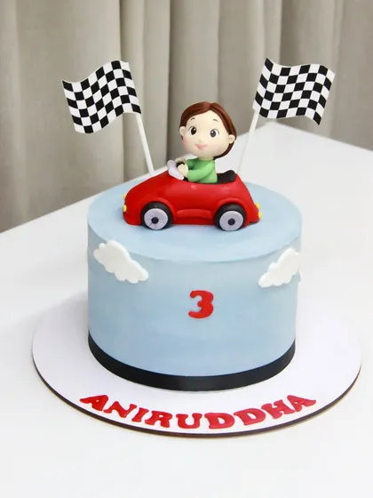A cute and simple car-themed cake for Aniruddha's 3rd birthday, featuring a little driver in his red convertible, ready to race.