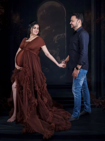A dramatic and romantic pose against a dark, moody backdrop. The couple holds hands, with the flowing brown gown adding a touch of elegance and movement to the scene.