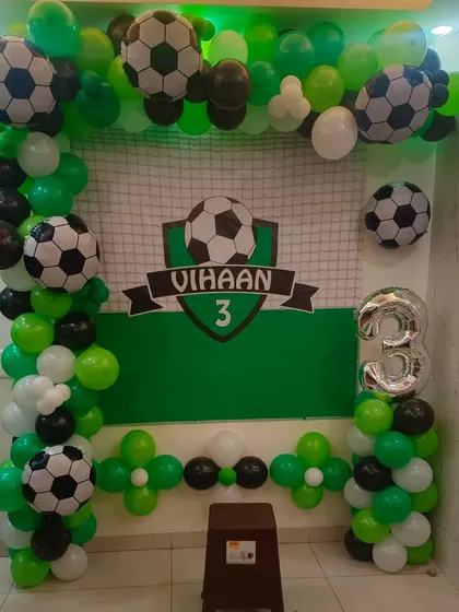 A football-themed decoration for a 3rd birthday. This setup includes a goal net backdrop, football-themed balloons, and a green, black, and white color scheme.