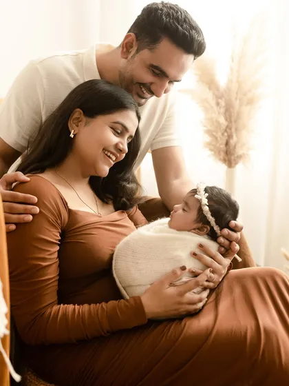 A joyful family photo with a newborn baby girl. The parents are all smiles as they admire their new daughter, swaddled cozily in the mother's arms.