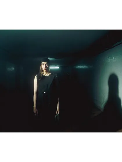 A minimalist shot in a dark hallway, where the model is almost a silhouette. The single light source and prominent shadow create a feeling of isolation and mystery.