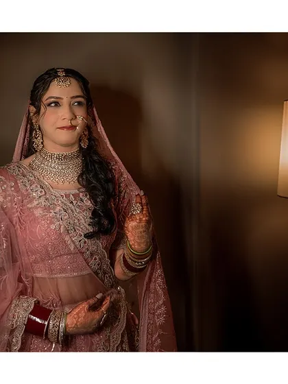 A classic bridal portrait. The soft lighting from the lamp creates a warm and intimate atmosphere, highlighting her beautiful pink lehenga.