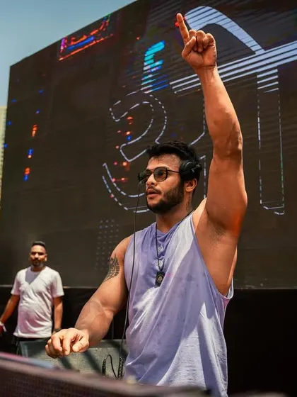 One hand up, connecting with the crowd at a daytime Holi festival. The massive LED screen behind me shows that I bring a full concert-level production to festive events.