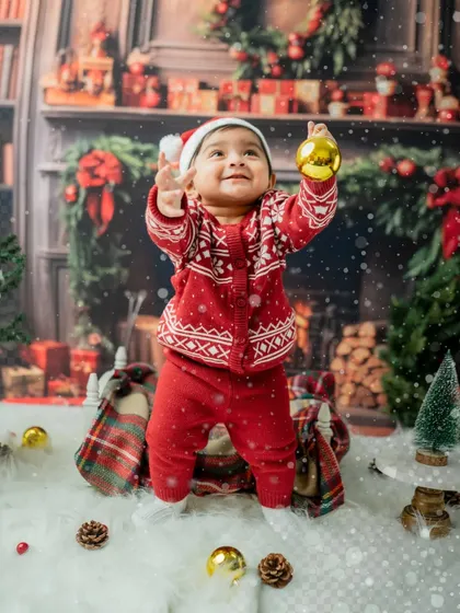Looking up with wonder, this toddler holds up a golden ornament. The lighting creates a magical, glowing effect.