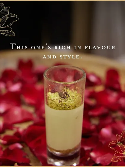 A layered pistachio dessert served in a shot glass against a bed of rose petals. This elegant presentation highlights the rich flavour and luxurious nature of the sweet.