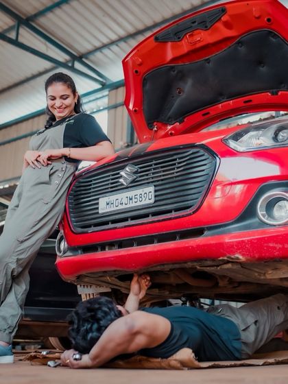 A fun, story-telling shot from a car garage themed shoot. The groom works under the car while his partner leans against it, creating a scene that's both playful and unique.