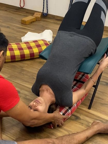 I am giving a gentle adjustment to a student's neck in a supported backbend over a chair. This ensures the neck is long and free of tension.