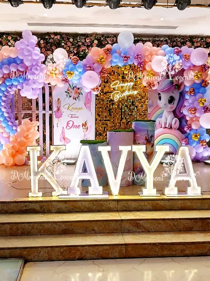 A variation of the unicorn-themed stage for Kavya's birthday. This setup includes a white picket fence element and a slightly different arrangement of the balloon rainbow.