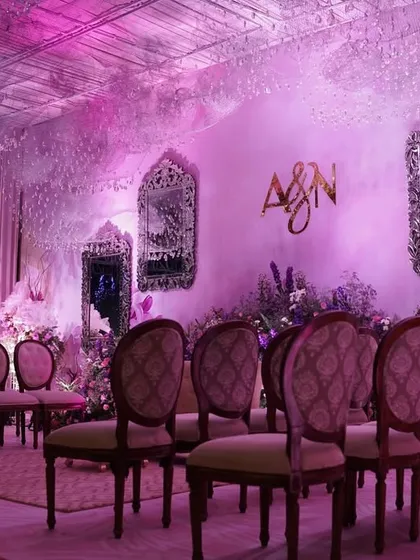 A beautiful seating arrangement for a ceremony, with vintage-style chairs facing a stage adorned with lilac florals, ornate mirrors, and a ceiling of cascading crystals.