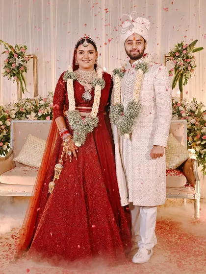 A classic portrait of the bride and groom after their wedding ceremony. Standing amidst a shower of petals, they look regal in their red and white attire.