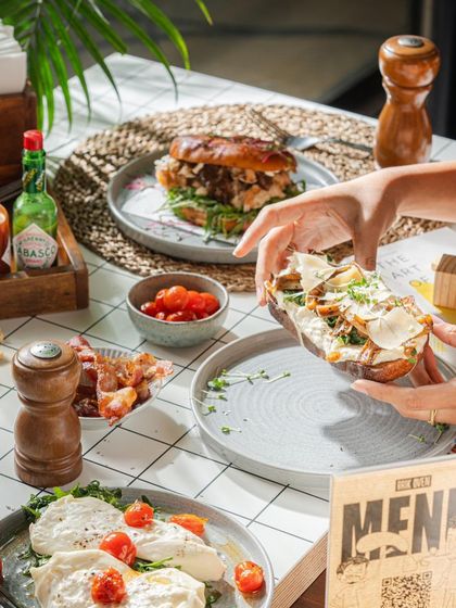 A shared breakfast moment, with hands reaching for different toasts and sandwiches from our deli menu.
